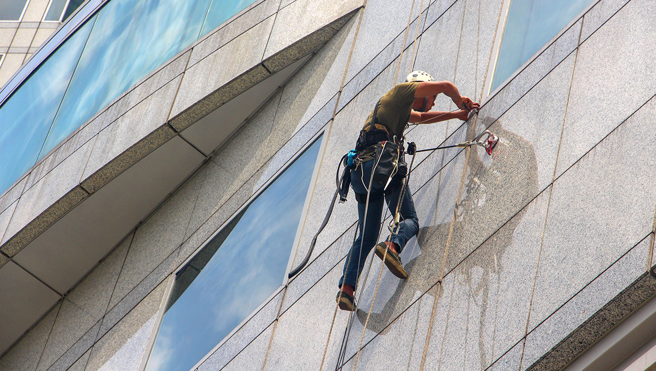 Man cleaning window Professional rope access cleaner using harness and safety equipment to wash building windows in Hertfordshire